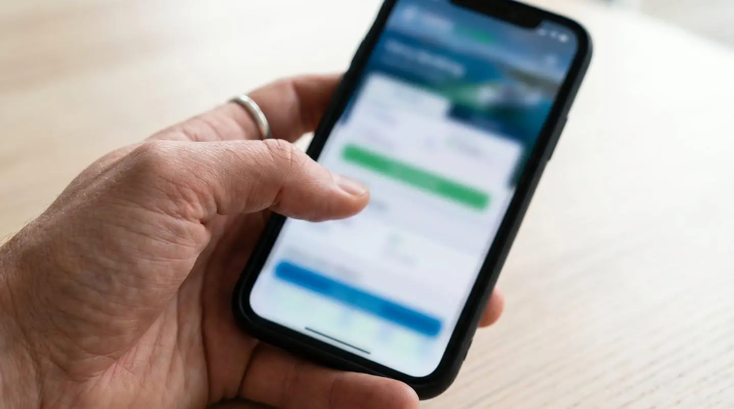 Gros plan d'une main tenant un smartphone affichant un écran de réservation ferry complètement flouté, avec un arrière-plan de table moderne en bokeh